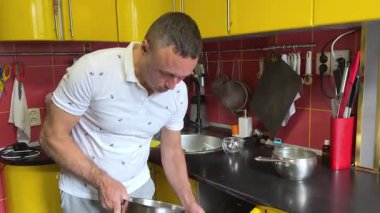 Dijital tablet üzerinde iletişim kuran neşeli adam sarı mutfakta yemek pişiriyor. Mutfakta tablet kullanan orta yaşlı bir adam internetten yemek pişirme süreci hakkında konuşuyor..