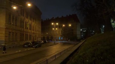 Eski taştan bir mahalledeki gölgeli cadde yumuşak fenerlerle aydınlanırken iki pencere rahatsız edici kırmızı ışıkla parıldıyor. Gecenin gizemli ve ürkütücü bir anını yaratıyor..