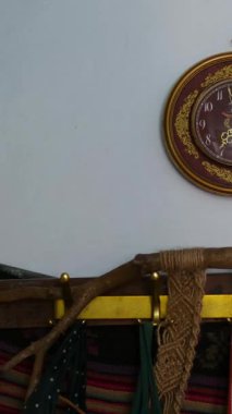 Seramik kireçlenmiş beyaz kireçlenmiş bir duvarın yanında duran eski soba, makrome ve antika bir saatle dekore edilmiş, rahat bir kırsal atmosfer yaratıyor..