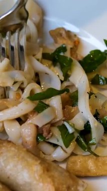 İki kızarmış Vietnam böreği, tatlı mısır ve beyaz tabakta geniş pirinç eriştesi. Erişte toplamak için çatal kullanan kadın eli. Hakiki Asya sokak yemeği..