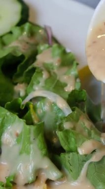 Salatalı taze salata, salatalık ve kremalı hardal tohumu soslu vişneli domatesler, iki yumuşak Vietnam çöreği ile birlikte beyaz bir tabakta servis ediliyor..