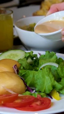 Salatalı taze salata, salatalık ve kremalı hardal tohumu soslu vişneli domatesler. Beyaz bir tabakta iki yumuşak Banh Bao buharlı çörekle servis ediliyor..