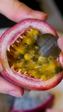 Genç bir kadının olgun tutku meyvesini tutarken ve çay kaşığıyla taze, sulu tohumları kepçelerken, masada tropik egzotik meyve hazırlarken, doğal gün ışığı sahnesinde..