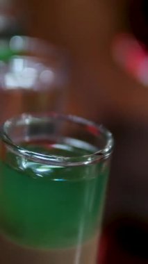 Becerikli barmen gece bir barda kokteyl hazırlıyor, sıcak ışık altında güzel kadehler oluşturmak için renkli içkiler döküyor. Yüksek kalite 4k görüntü