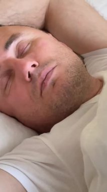 Genç ve yakışıklı bir adam yatakta uykusundan esneyerek ve mutlu uyanır. Adam harika bir uyku çekti. Uyku ve dinlenme için uygun koşullar. İyi sabahlar. Yeni bir günün başlangıcı.