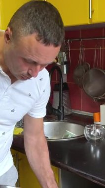 Dijital tablet üzerinde iletişim kuran neşeli adam sarı mutfakta yemek pişiriyor. Mutfakta tablet kullanan orta yaşlı bir adam internetten yemek pişirme süreci hakkında konuşuyor..