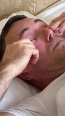 Kafkasyalı bir adam yatağında uzanmış gözlerini ovuşturarak uyanıyor. Erkek yatak odası, uykulu uykulu, uyanık. Rahat bir yeni gün ev sahibi. .