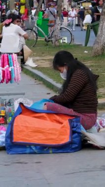 Hoi An 'daki Vietnamlı kadın kaldırımda oturmuş el işi el sanatları satıyor yüz maskesi takıyor ve yerel kültürün ve günlük hayatın özgün olduğunu gösteriyor.