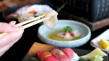 Çubuklar, parlak stüdyo ışıkları ve siyah arka plan altında ton balığı sashimi, salatalık ve shiso yaprağı ile bir tabak somon balığı sashimi kaldırır. Yüksek kalite 4k görüntü