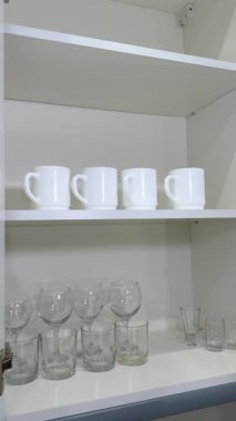 Ahşap elementler ile minimalist iç tasarım uyumu vurguluyor düzenlenmiş bardaklar ve kupalar rahat bir atmosfer yaratıyor raf merkezi bir element haline geliyor düzeni kuruyor ve yansıtıyor .