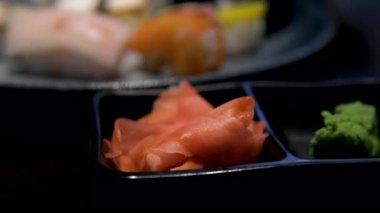 Nigiri, somon ruloları, turşulu zencefil, wasabi ve taze garnitürlerden oluşan siyah bir tabakta çok güzel düzenlenmiş suşi tabağı. Canlı ve iştah açıcı bir Japon yemeği. Yüksek kalite 4k görüntü