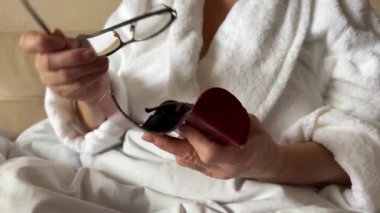 Yakın plan portre: yaşlı kadın yüzüne gözlük takıyor. Son sınıf dişisi görüşünü düzeltmek için gözlük kullanıyor. Yaşlı bayanın sivilceli kuru kötü bir teni var. Optik konsept, mavi gözler, uzun gri saçlar.