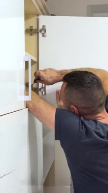 Adam modern dolapta tornavida kullanarak mutfak çekmecesini monte ediyor. Tamirci, çağdaş mutfağa çekmece kaydırma mekanizması kuruyor ve ayarlıyor. Mobilya döşemesi. Yüksek kalite 4k