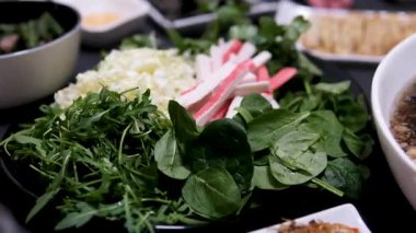 Tabakta yeşiller, ıspanak, roka, Çin lahanası ve yengeç çubukları var. Açık büfedeki taze salata tabağına renkli sebze malzemesi ekleyen müşterinin genel görünümü. Yüksek kalite 4k