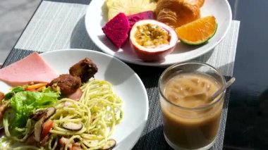 Asya omletinde kahvaltı, kızarmış yumurta, erişte, makarna, yeşillik, sebze, kahve bardakta, tutku meyvesi, ejderha meyvesi, mandalina ve lüks bir otelin balkonundaki bir masada hamur işleri..