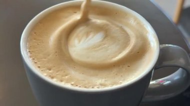 Ahşap bir sopayla gri bir fincanda latte cappuccino kahvesi karıştırıyorum. Yüksek kalite 4k görüntü