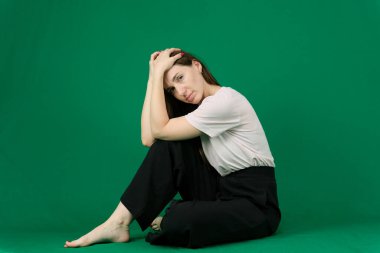 Farklı pozlarda uzun kahverengi saçlı, yeşil arka planda pembe tişörtlü ve siyah pantolonlu Avrupalı bir kadının çeşitli duyguları. Yüksek kalite fotoğraf