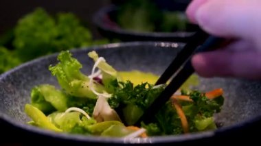 Asyalı adam yakın plan kağıt tabaklardan taze salata yiyor. Gezegeni temizlemek için modern trendleri desteklemek için çubuklar kullanıyor. Sıfır atık yiyecek için tek kullanımlık kağıt masatakımı.