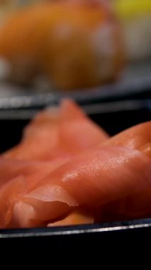 Nigiri, somon ruloları, turşulu zencefil, wasabi ve taze garnitürlerden oluşan siyah bir tabakta çok güzel düzenlenmiş suşi tabağı. Canlı ve iştah açıcı bir Japon yemeği. Yüksek kalite 4k görüntü