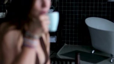 Kadın eli bir fincan kahve alıyor, sonra kadın siyah yuvarlak masanın yanındaki gri koltuğa oturuyor. Asyalı tarzı iç mekan, sakin yaşam tarzı ve rahat bir yuva anı..