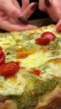 Taze domatesli, peynirli ve fesleğen yapraklı dikdörtgen pizza, yakın çekim görüntüsü. Bir kız pesto soslu bir dilim pizza alır. İtalya 'da dikdörtgen bir pizza..