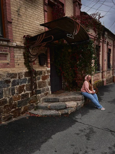 Resimde sonbahar ormanında yürüyen bir kız görebilirsiniz, sarı yapraklı ağaçların arasında yürüyen şapkalı bir kız..