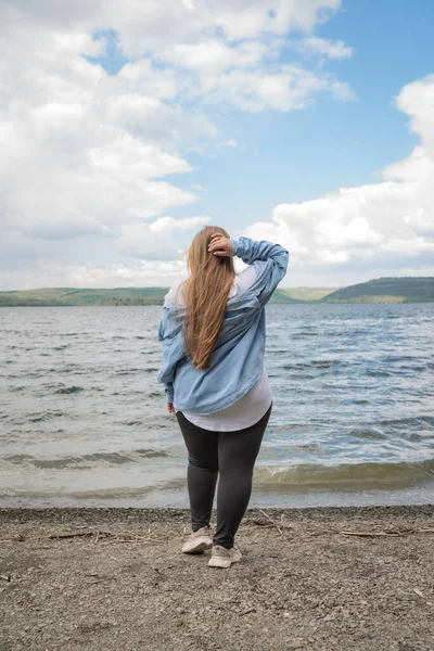 Uzun saçlı kız gölün arka planında poz veriyor.