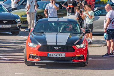Beyaz çizgili siyah Ford Mustang, halka açık bir yere park edilmiş, birden fazla kişi gözetliyor, bazıları akıllı telefon kullanıyor. Backgrou Kyiv, Ukrayna - 21 Eylül 2025