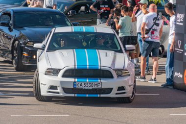 Özel bir etkinlik sırasında mavi ve beyaz bir Ford Mustang spor arabası bir şehir sokağına park edilmiş, kalabalık kamerasız Kyiv, Ukrayna - 21 Eylül 2025