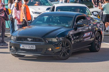 Siyah, cilalı bir Ford Mustang caddede çapraz park halindedir. Arka planda bulunan plaka ve yayalar, Pu Kyiv, Ukrayna - 21 Eylül 2025
