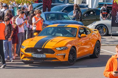 Açık hava otomobil fuarı, Vibrant turuncu Ford Mustang kaslı araba, Siyah çizgili, Seyirciler, Derinlik, Doğal ışıklandırma, Gün Işığı, Hafifçe yükseltilmiş perspektif, Motion, Kyiv, Ukrayna - 21 Eylül 2025