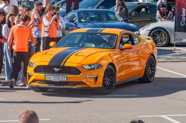 Açık hava otomobil etkinliklerindeki çeşitli kalabalıkların arasında, siyah şeritli parlak sarı Ford Mustang GT arabası ana odak noktası. Sahne, Natur Kyiv, Ukrayna - 21 Eylül 2025