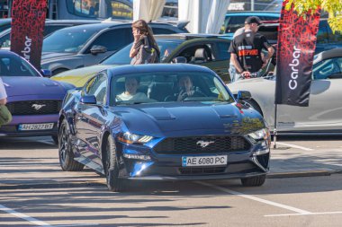 Mavi Ford Mustang GT, sağ tarafta park halinde, çeşitli araçlarla çevrili ve insanlar onları hayranlıkla izliyor ya da tartışıyorlar doğal Li Kyiv, Ukrayna - 21 Eylül 2025