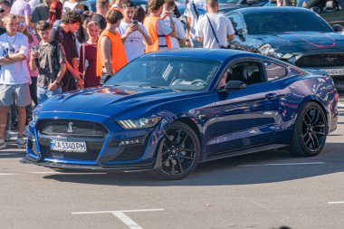 Ukrayna 'nın başkenti Kyiv' e karşı çeşitli faaliyetlerde bulunan insanlar tarafından çevrelenmiş mavi Ford Shelby GT500 AM83HN 'nin yer aldığı gece otoparkı sahnesi - 21 Eylül 2025