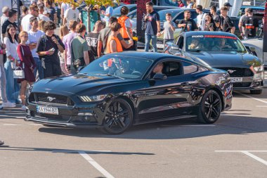 Dikey bir panoramik görüntü, insanların olduğu bir açık hava sahnesi gösteriyor, muhtemelen bir halk toplantısı, ve Ukrayna 'nın en alt yarısında siyah bir spor araba - 21 Eylül 2025