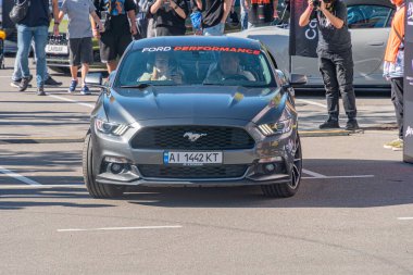 Siyah Ford Mustang, yarışmada piste park edilmiş, sürücü koltuğundaki kişi, bir grup seyirci ya da takım üyesi, günlük ve spor kıyafetleri, açık hava ayarı, parlak Kyiv, Ukrayna - 21 Eylül 2025