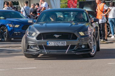 Siyah Ford Mustang 'in yarış çizgileri parlak bir sokak sahnesine park edilmiş, açık gökyüzünün altında arka planda günlük kıyafetler giymiş insanlar Kyiv, Ukrayna - 21 Eylül 2025