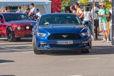 İki klasik Ford Mustang, bir kırmızı üstü açık ve bir koyu mavi fastback, güneş ışığı altında bir araba fuarında üstü açılabilir kırmızı iç açıcı beyaz çadırda Peo Kyiv, Ukrayna - 21 Eylül 2025