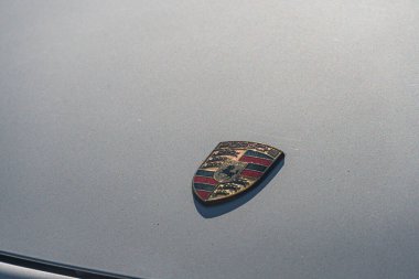 Siyah ve gümüş çizgili gümüş bir kalkanla oval alanda bulunan metalik bir araç panelinin üzerinde canlı kırmızı bir Porsche amblemi var. Arka plan Kyiv, Ukrayna - 21 Eylül 2025