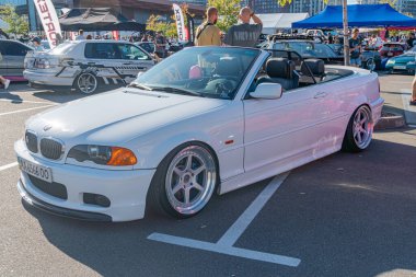 Beyaz BMW E30 'lu canlı bir araba gösterisi sahnesi, asfalt yüzeyinde yapay ışıkların altında parlayan klasik model. Arabanın üstü siyah yumuşak ve Kyiv, Ukrayna - 21 Eylül 2025