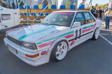 Çok renkli, pembe, mavi, mor renkli bir yarış arabası, bir numaralı endüstriyel katın üzerine park edilmiş Rally ve RRT insanlarını da kapsıyor. 21 Eylül 2025