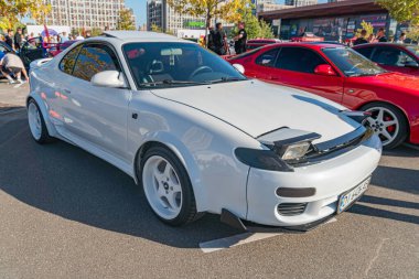 Bir araba fuarında özel beyaz spor araba, asfalt parkında süs, geniş duruş, geniş gövde kiti, büyük tekerlekler performans modifikasyonlarını gösteriyor.