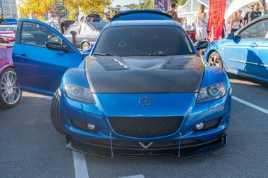 Şov ışıkları altında merkezi, çarpıcı mavi bir spor arabanın yer aldığı, aerodinamik tasarım unsurlarının sergilendiği ve sessiz Kyiv, Ukrayna 'ya karşı kontrastlı bir araba fuarından canlı bir sahne - 21 Eylül 2025