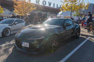 Siyah, parlak Toyota Supra açık araba meraklısı Parlak güneşli bir gün, çeşitli arabalarla döşeli bir alan ve Kyiv, Ukrayna hakkında konuşan insanlar - 21 Eylül 2025