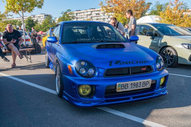 Canlı mavi Honda Integra Tipi R Aerodinamik gövde kiti ve arka kanat ile, asfaltlı bir otoparkta açık mavi gökyüzüne karşı Kyiv, Ukrayna 21 Eylül 2025 'de etrafa saçılmış insanlar