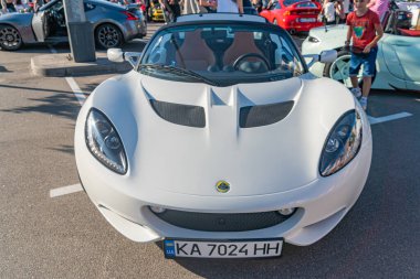 Geniş hava girişli ve düz gövdeli beyaz spor araba, KA KA 7026 H NH plakalı, kapalı bir park alanında veya sergi salonunda diğer arabalar Kyiv, Ukrayna 'da görülebiliyor - 21 Eylül 2025