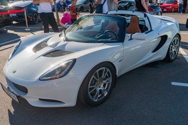 Aerodinamik hatları ve geniş hava girişleriyle halka açık bir caddeye park edilmiş beyaz Lotus arabası. Çevredeki ışığı yansıtan Glossy finansman kapısı sh Kyiv, Ukrayna - 21 Eylül 2025