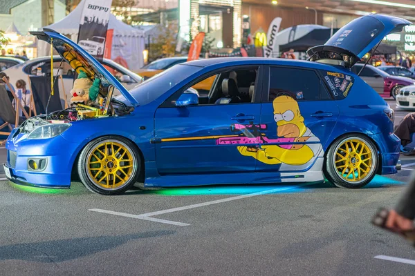 Sarı jantlı canlı mavi araba, ayırt edici vücut kiti, açık kaput, motor görünür, Homer Simpson çıkartması, açık hava anteni, doğal gün ışığı, yükseltilmiş açı Kyiv, Ukrayna - 21 Eylül 2025