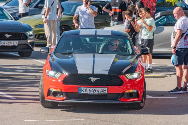 Beyaz çizgili siyah Ford Mustang, halka açık bir yere park edilmiş, birden fazla kişi gözetliyor, bazıları akıllı telefon kullanıyor. Backgrou Kyiv, Ukrayna - 21 Eylül 2025