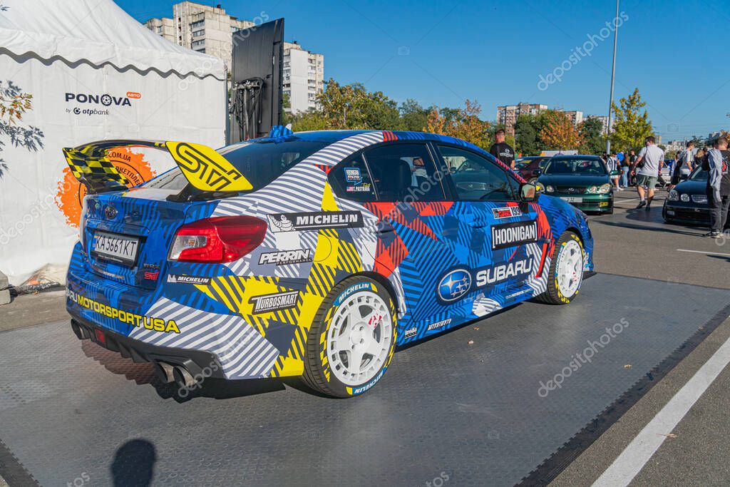 Side view of a vibrant, sponsored racing car at an outdoor automotive event on a tarmac Aerodynamic design with rear spoiler and track-optimized mirrors Bright blu Kyiv, Ukraine - September 21, 2025